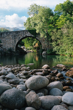 Stone arch bridge over calm river with rocky shore