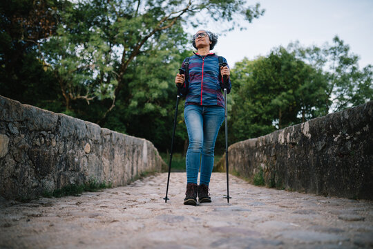 Woman hiking with trekking pole on stone bridge in nature