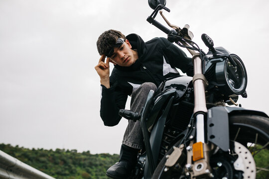 Man with motorcycle on open road under cloudy sky
