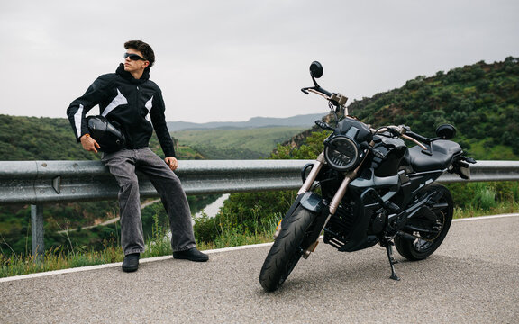 Man with motorcycle on road overlooking green valley