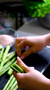 Female hand trimming fresh asparagus by snapping off tough ends before cooking preparing tender green spears for healthy homemade meals and simple recipes