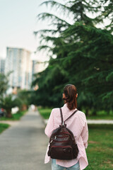 Naklejka premium Woman with backpack walking along a park path, casual outfit in an outdoor setting, capturing lifestyle and urban nature in a candid moment, sunny mood