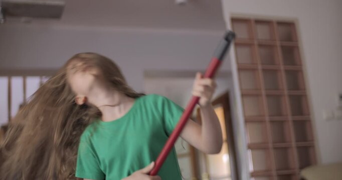Enjoying Cleaning Playful Creative Child Dancing. Creative Teenage Girl Housewife Cleaning and Singing Using Broom Handle as Guitar Child Using Mop as Musical Instrument While Singing in Home.