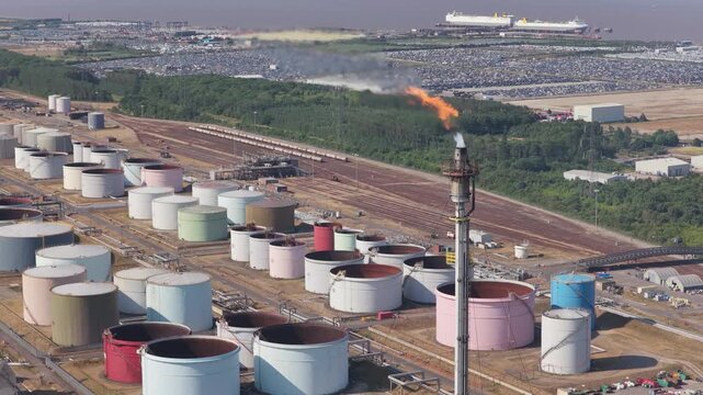 Industrial Refinery Flare Stack Burning Gases at Large Storage Tank Facility During Day