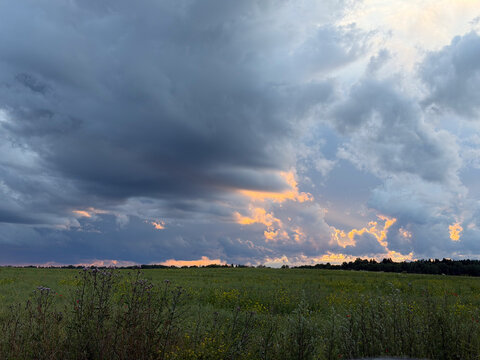 Clouds gather over a field as sunset light breaks through during late evening in a rural area
