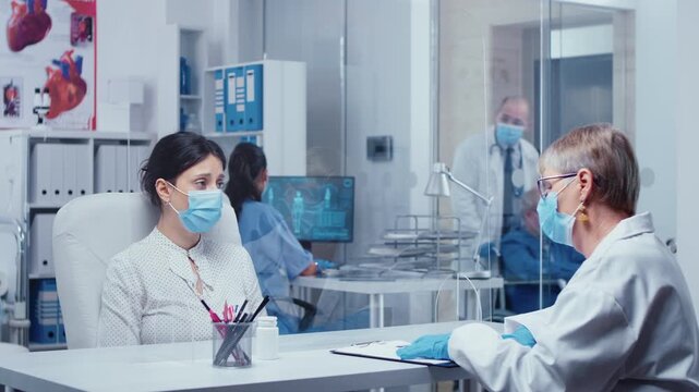 Woman wearing a protective mask cries after receiving bad news from a doctor through a plexiglass wall during a protected consultation.