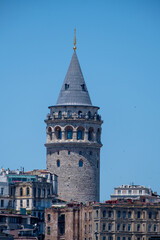 Naklejka premium Galata Tower Rising Between Historic Buildings in Istanbul. Historic Galata Tower Surrounded by Istanbul Buildings. Galata Tower Emerging Above the Cityscape.