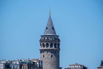 Naklejka premium Galata Tower Rising Between Historic Buildings in Istanbul. Historic Galata Tower Surrounded by Istanbul Buildings. Galata Tower Emerging Above the Cityscape.