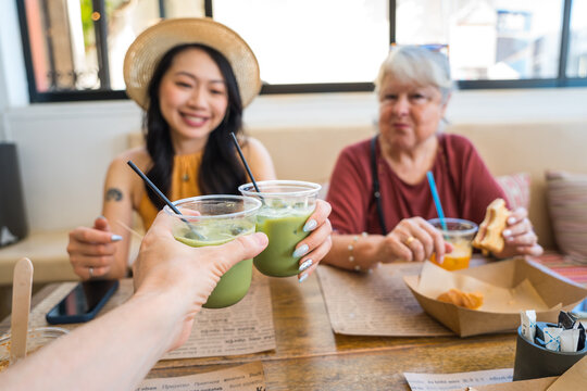 Friends toasting iced matcha lattes at a cafe table