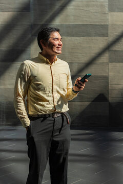 Smiling Asian man using smartphone in sunlit corridor