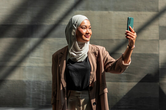 Young woman in hijab taking a selfie in urban sunlight