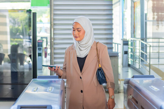 Muslim woman using smartphone at station ticket gate