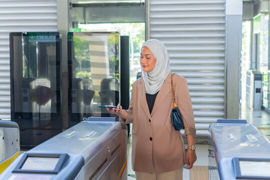 Muslim woman using smartphone at station ticket gate