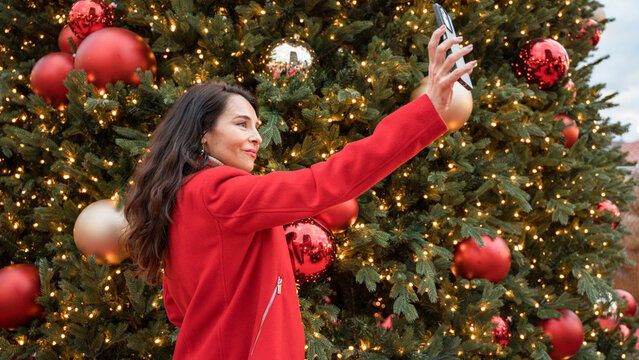 Woman taking selfie by decorated Christmas tree lights