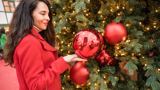 Woman in red coat touching Christmas ornament on tree