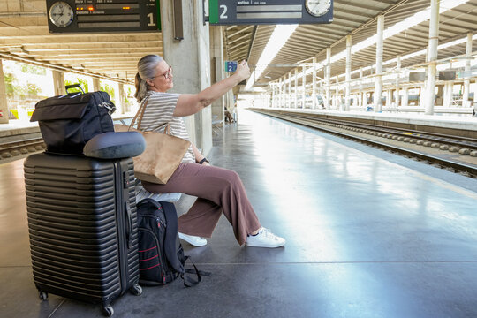 Mature woman capturing travel moment on train platform