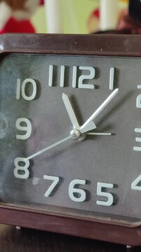 A detailed shot zooms out from a square brown analog clock face with silver hands ticking steadily. Concept of deadline pressure, schedule management, and the unstoppable passing of time.