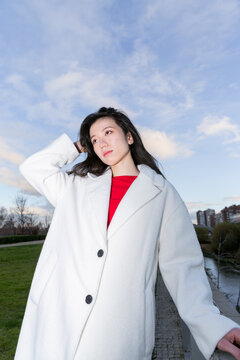 Gen z Asian woman in white coat posing outdoors at dusk