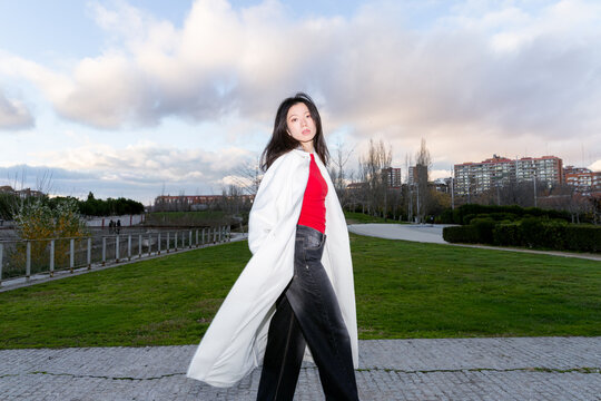 Gen z asian woman posing outdoors in urban park at dusk