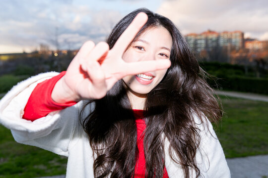 Gen Z Asian woman flashing peace sign in city park