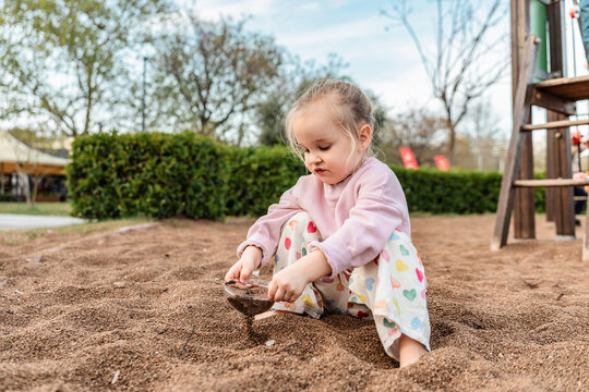 Toddler playing with sand on playground in sunny park