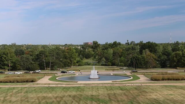 Circular fountain in park with surrounding grass and trees.