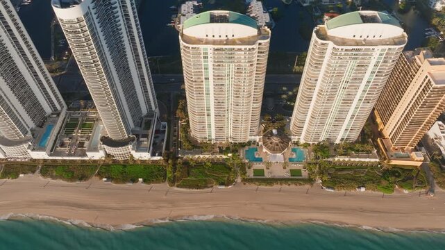 Stunning aerial perspective of Sunny Isles Beach in Miami showcasing luxury high-rise condominiums along the Atlantic Ocean shoreline with rooftop pools and sandy beach during golden hour light.