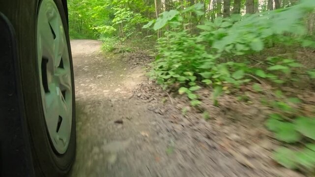 Rural countryside road in the woods drive on the gravel. Cinematic POV of front right car wheel driving plate. Gentle turns on dirt road in the crown land from behind right wheel exterior view.