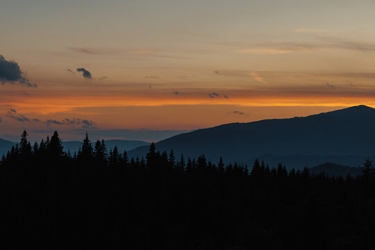 Beautiful evening twilight with bright orange sky above dark mountain ridges.