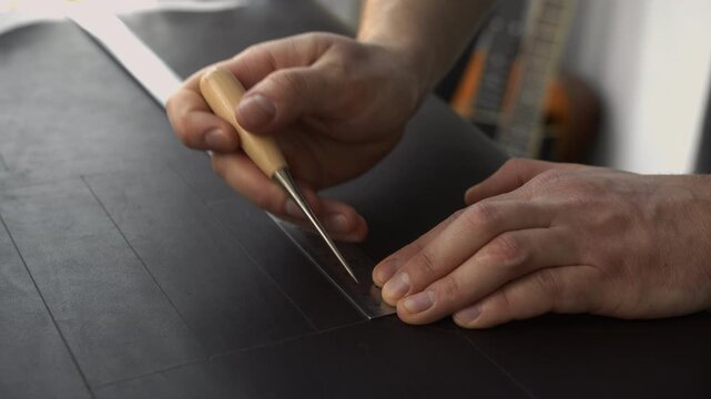 Craftsman working on black leather using a ruler and awl for cutting precise patterns in a workshop
