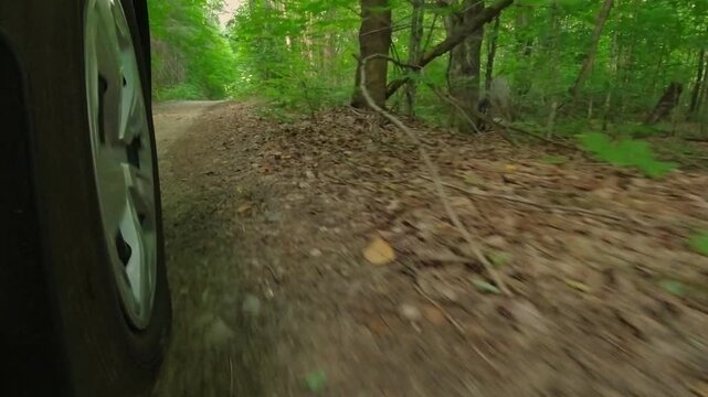 Rural countryside road in the woods drive on the gravel. Cinematic POV of front right car wheel driving plate. Gentle turns on dirt road in the crown land from behind right wheel exterior view.