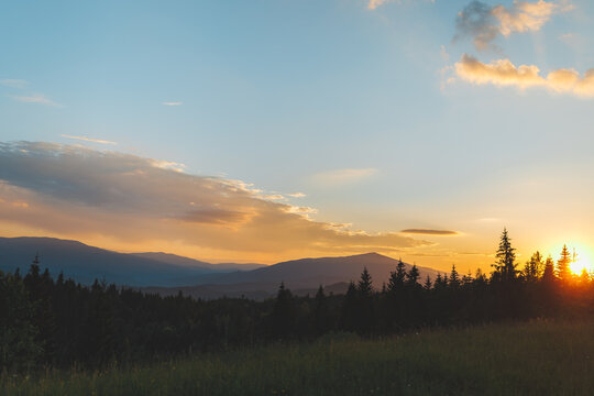 Beautiful sunset over the Carpathian mountains with sun rising or setting behind pine trees.