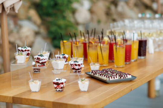 Catering buffet table with sweet mini desserts in cups and refreshing cocktails.
