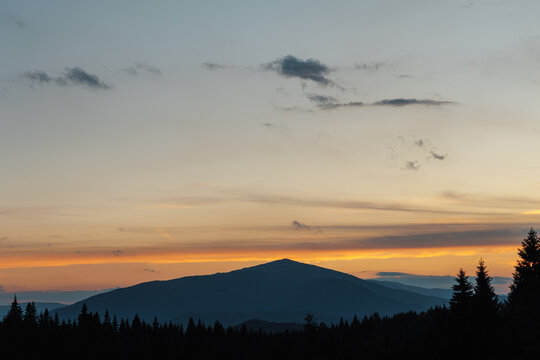 Beautiful evening twilight with bright orange sky above dark mountain ridges.