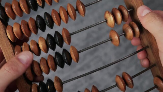 A close-up view of hands holding and moving beads on a vintage wooden abacus. Concept of traditional accounting, financial mathematics, history of calculation, and educational tools.