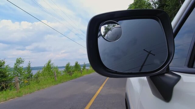 Frame with cars side mirror during the travel on the cottage country rural road in North America. Half view of side rear view mirror of a car driving along the highway, and half of road and nature.