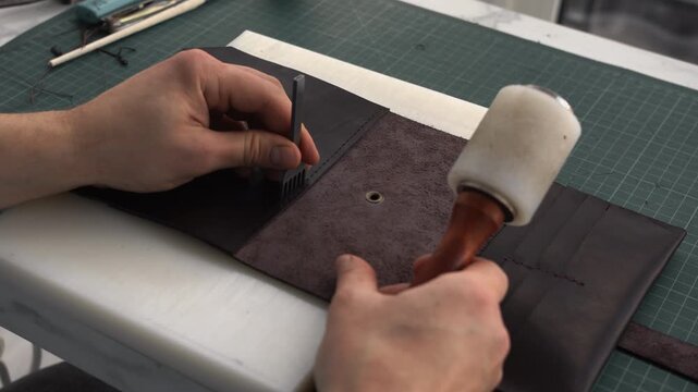 Leatherworker punching holes in a handmade wallet using a stitching chisel and maul for saddle stitching