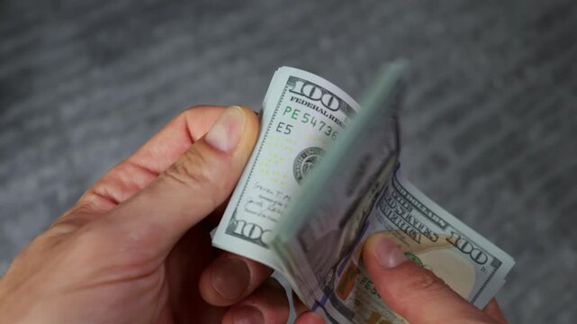 A close-up view shows male hands counting a stack of crisp one hundred US dollar bills. Concept of financial success, wealth management, cash payment, and banking transactions.