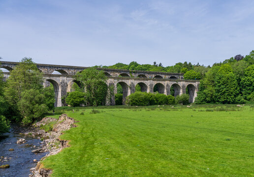 Two people walk in a field below the impressive Chirk Aqueduct and Viaduct, a UNESCO World Heritage site in rural Shropshire.
