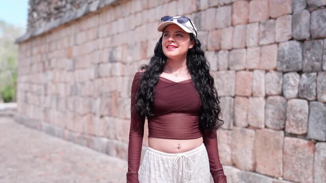 Young Latina woman exploring the archaeological site of Uxmal in Yucatan Mexico, walking next to an ancient Mayan stone wall, enjoying history, culture, and travel in a UNESCO heritage destination