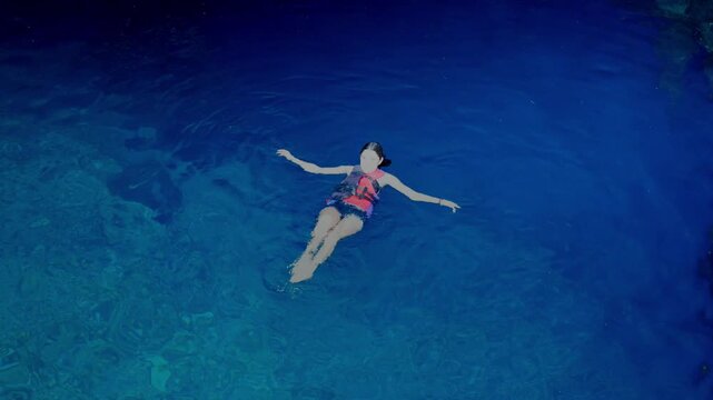 Young smiling Latina woman relaxed and adventurous while floating and swimming in a deep blue cenote in Yucatan Mexico, surrounded by clear freshwater and rocky walls, wearing life jacket and swimwear