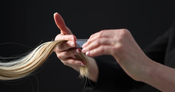 Hairdresser spraying and combing client's hair on black background, closeup
