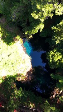 Aerial vertical top down tracking shot moving over a deep blue clear water lagoon surrounded by dense green forest