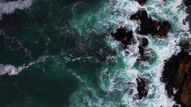 Drone Horizontal Stationary Top Down View of Ocean Waves Churning and Splashing Over Dark Reef Rocks, Chile