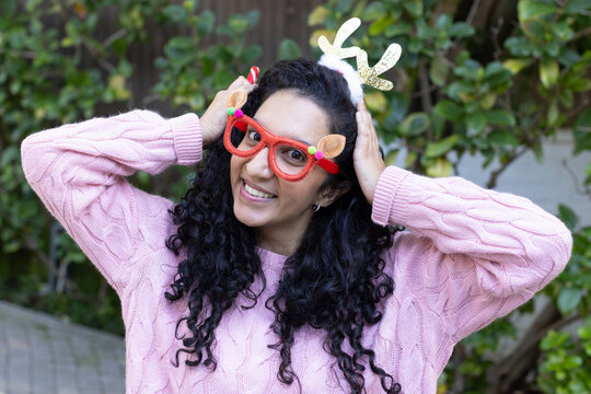 African American woman wearing pink sweater holding antler headband and reindeer glasses in garden