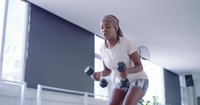 Starting from squat, woman wearing head wrap lifting dumbbells, moving upright, building strength