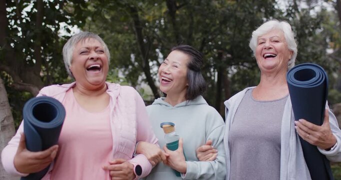 Diverse female friends with senior linking walking park sharing glance laughing holding mats bottle