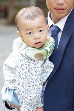 Softly dressed baby held close to adult. Baby gazes curiously at camera with wide eyes. Adult's expression gentle, softly smiling. Ideal for family, parenting, or newborn themes
