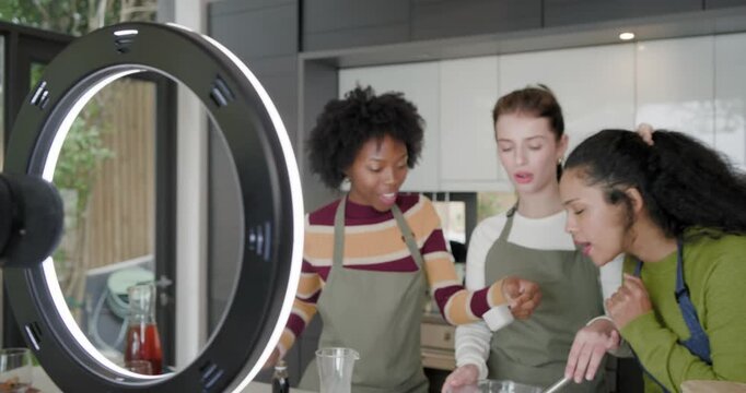 Diverse female friends in aprons mixing batter in bowl, kitchen island, camera rolling for tutorial