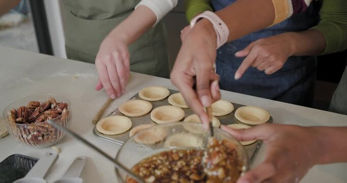 Diverse female friends spotting prebaked shells, scooping pecan caramel into cups at home for tarts
